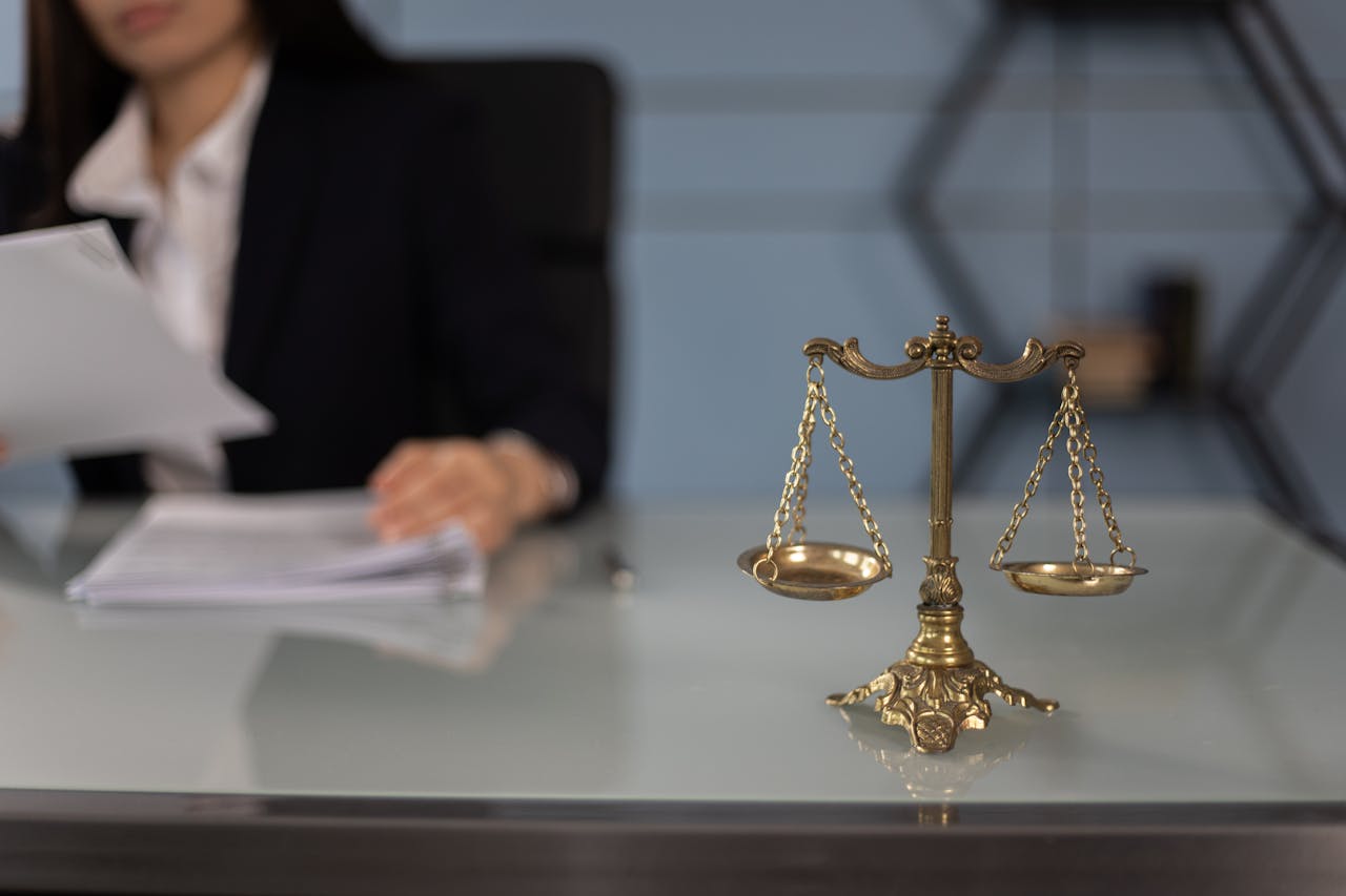 about-us Balance scales on a desk in a professional office with a blurred businesswoman in the background.